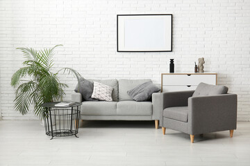 Interior of stylish living room with grey sofa, armchair and blank frame
