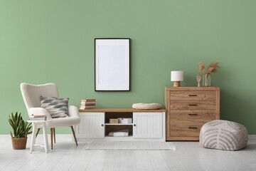 Interior of stylish room with white armchair, dresser and blank frame