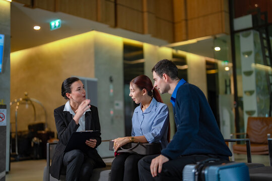 Professional hotel staff talking with guests in lobby area, providing travel information and service consultation for international tourists, concept of hospitality and business travel meeting.