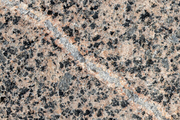 Spotted granite stone texture, close up view with a white vein line
