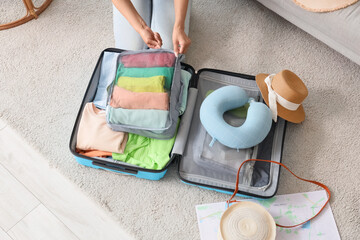 Young woman with organizer packing clothes into suitcase for trip at home. top view