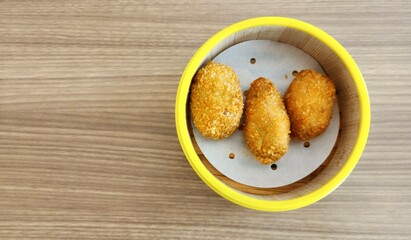 Three pieces of cheese shrimp dim sum (one of the popular snacks in Indonesia) in a minimalist round wooden container on the table.