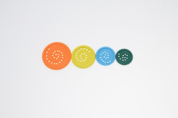 colorful plastic gears, arrangement arranged in a line orange, yellow, blue, and green ideal for educational materials, science learning visuals, creative business concept isolated on white background
