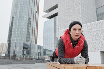 Young determined Caucasian woman in warm sportswear doing plank and listening to music while having...