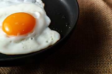 Fried egg sunny side up in a dark frying pan on burlap fabric