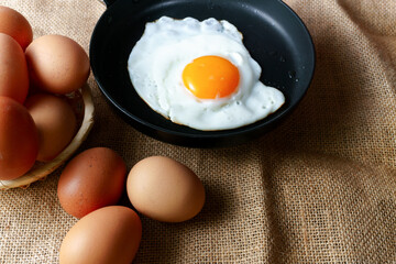 Fried egg cooking in a black pan next to brown farm fresh eggs on rustic burlap
