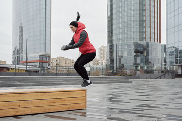 Determined young Caucasian woman doing jumping exercise while having outdoor workout in city center...