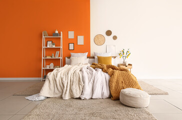 Interior of stylish bedroom with cozy bed, shelving unit and lemon tree branches on bedside table