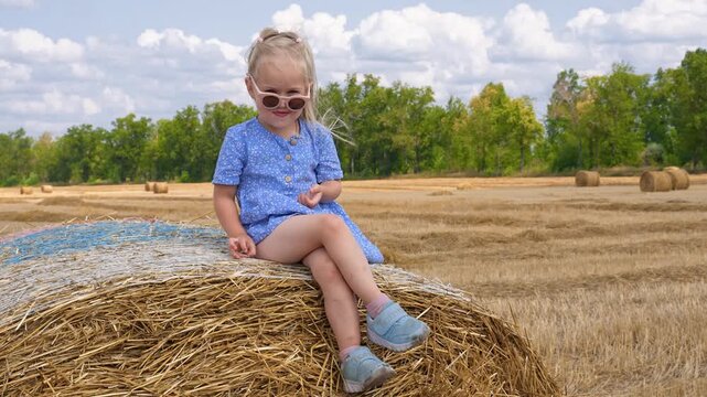 Cute little child sits on a haystack in a rural field in summer