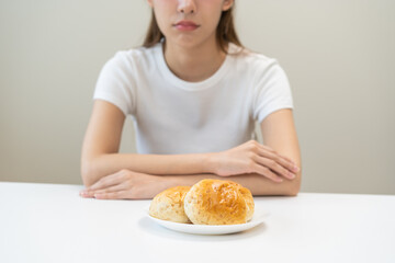 Gluten allergy, asian young woman, girl refusing to eat, looking at bread slice on plate in breakfast food meal on table at home, having a stomach ache. Gluten intolerant and Gluten free diet concept.