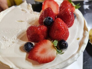 Close up shot of fresh strawberries and blueberries on a cake topped with cream