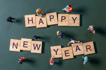 Miniature figurines surrounding wooden letter tiles forming the phrase Happy New Year