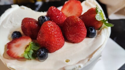 Close up shot of fresh strawberries and blueberries on a cake topped with cream
