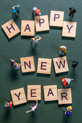 Miniature figurines surrounding wooden letter tiles forming the phrase Happy New Year