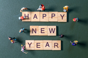 Miniature figurines surrounding wooden letter tiles forming the phrase Happy New Year