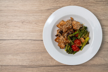 Stir-fried red snapper with teriyaki sauce and various vegetables: broccoli, tomatoes, asparagus, and baby corn on wooden table, Top view.