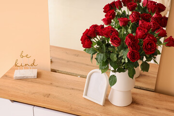 Vase with beautiful red roses and mirror on table in stylish room, closeup