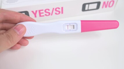 Woman's hand holding a home pregnancy test stick showing a positive result