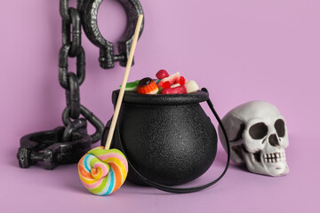 Cauldron of tasty jelly candies, skull and chain on lilac background