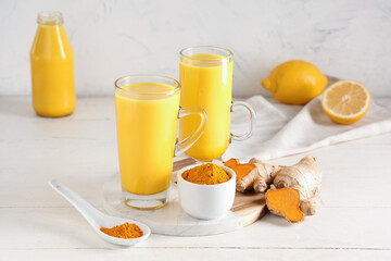 Glasses of healthy turmeric drink and ingredients on white wooden background, closeup
