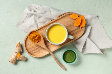 Composition with tray, cup of healthy turmeric drink and ingredients on light green grunge background