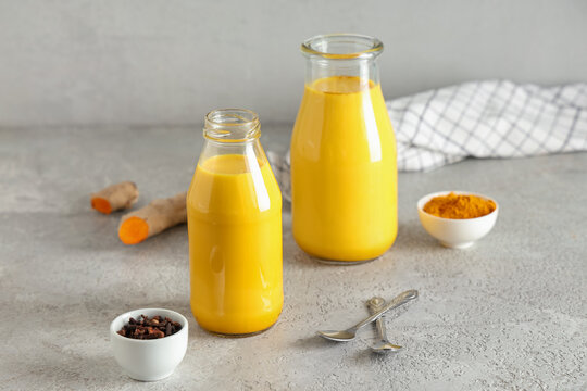 Composition with bottles of healthy turmeric drink and ingredients on grey grunge background, closeup