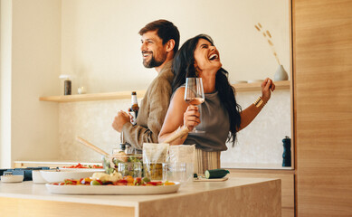 Happy couple enjoying wine while cooking and dancing in a cozy home kitchen