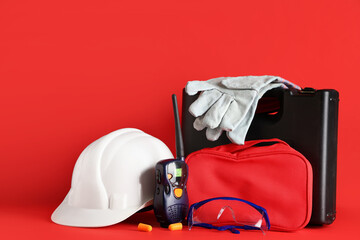 Hardhat, first aid kit, tool box and radio transceiver on red background