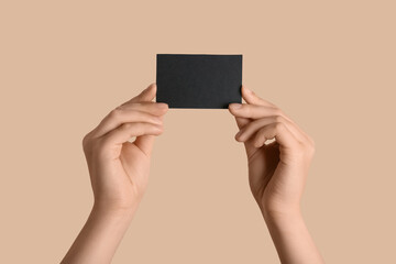 Female hands with blank black business card on beige background
