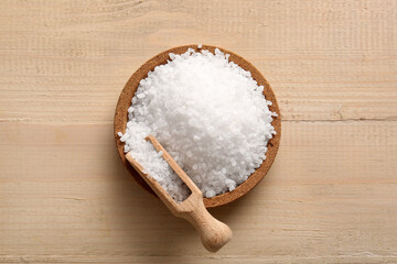 Plate with sea salt and scoop on wooden background