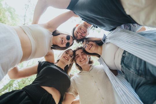 A diverse group of young friends sharing joy and laughter outdoors during a sunny day. - Powered by Adobe