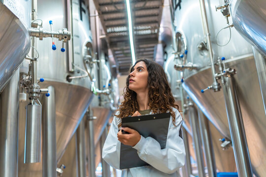 Woman inspecting beer fermentation tanks in brewery factory
