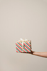 Hand holding a beautifully wrapped striped Christmas gift with a white bow