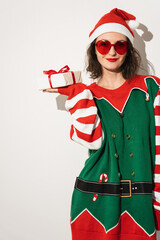 Woman in festive elf outfit with sunglasses holding miniature wrapped Christmas gift