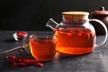 Glass cup and teapot of hot goji tea on dark background