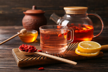 Glass cup of hot goji tea with lemon and bowl of honey on wooden background