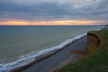 Orange sunset on the sea. Bright juicy landscape with feathery clouds on the horizon. Purple, lilac, pink shades of the evening sky. A calm turquoise sea rolls onto the beach. Idyll, relaxation