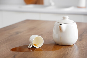 Overturned cup, pot and spilled coffee on table in kitchen