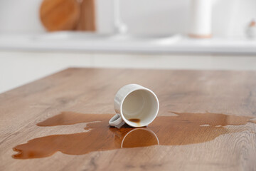 Overturned cup and spilled coffee on table in kitchen