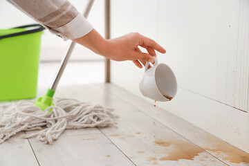 Woman picking up overturned cup of coffee from floor in kitchen