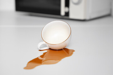 Overturned cup and spilled coffee on table in kitchen, closeup