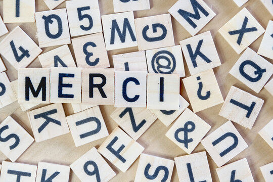 Wooden tiles with black letters and numbers scattered on a table, forming the French word "MERCI" in the center, meaning "thank you."