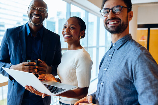 Three professionals discussing work while smiling and holding a laptop
