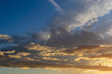 Fototapeta premium Layers of golden clouds illuminated by the setting sun against deep blue sky