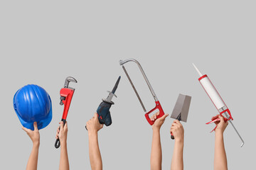 Hands with hardhat and construction tools on grey background