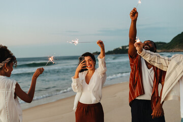 Group of friends celebrating with sparklers on a scenic beach at sunset