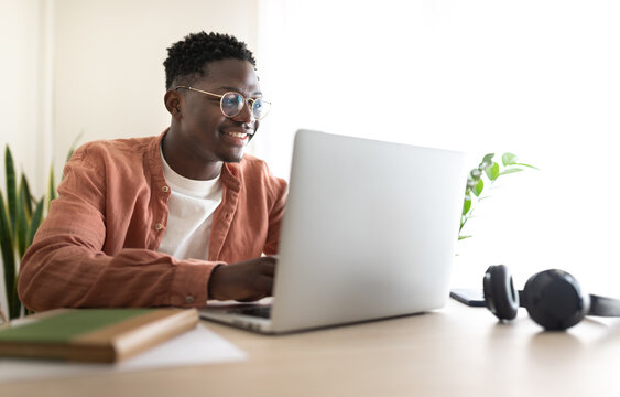 Smiling young man working from home office using laptop computer - Powered by Adobe