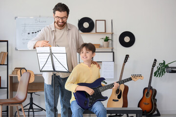 Private music teacher with note sheet giving guitar lessons to boy in room