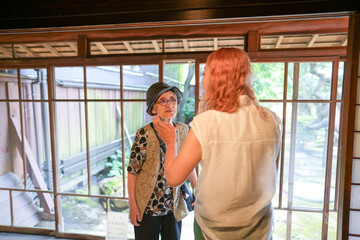 Fototapeta premium A woman in a white shirt is talking to an older woman in a hat. The older woman is holding a purse