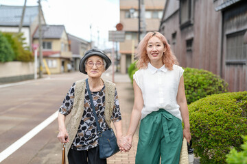 Naklejka premium Two women walking down a street, one of them is wearing a hat. The woman in the hat is holding the hand of the woman in the white shirt